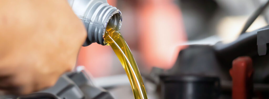 Oil poring from a jug into a vehicle engine.