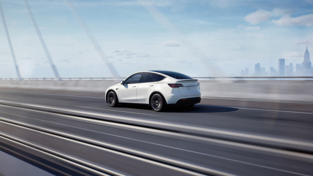 Image showcasing driver rear quarter profile of the Tesla Model Y on highway bridge